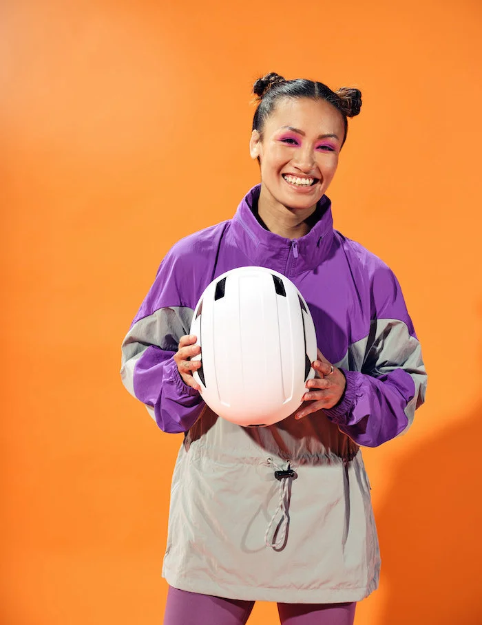 Female dressed in bright coloured clothing holding white bicycle helmet and smiling at camera.