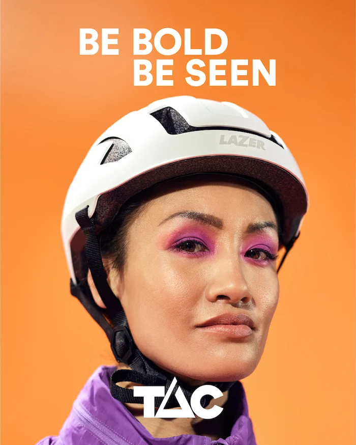 Female wearing white bicycle helmet and looking at the camera. Be Bold. Be Seen. TAC.